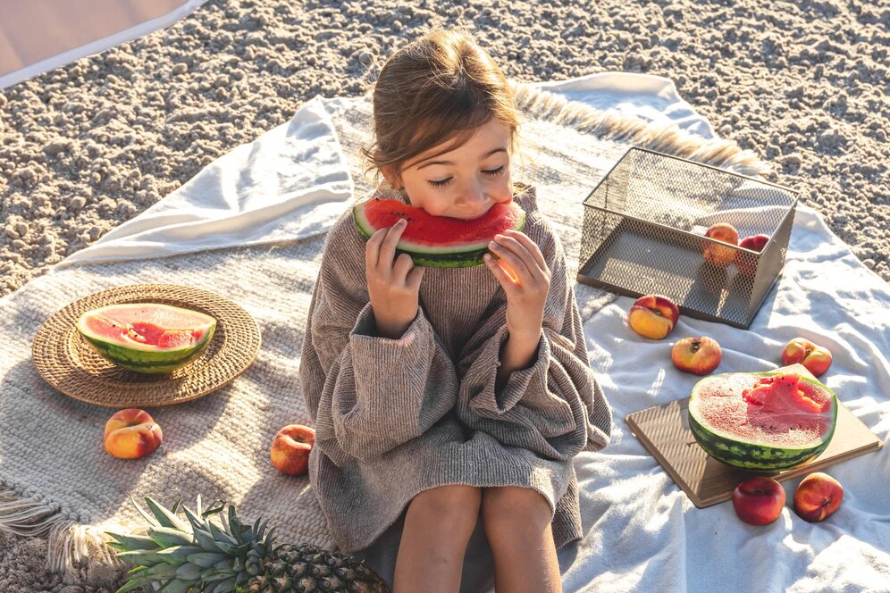 Fille mangeant une tranche de pastèque sur la plage, symbole d'été